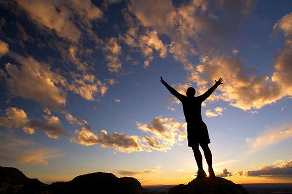 Man standing with arms outstretched against a sky full of clouds