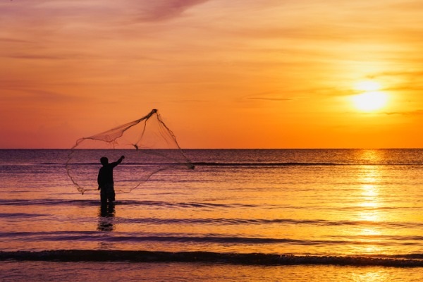 Silhouette of fisherman throwing fishing net in morning at tropical picture. 