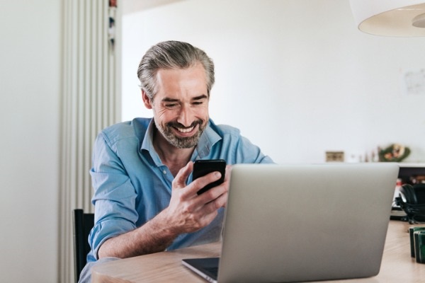 happy-bearded-business-man-looking-at-mobile-in-front-of-laptop-picture-id