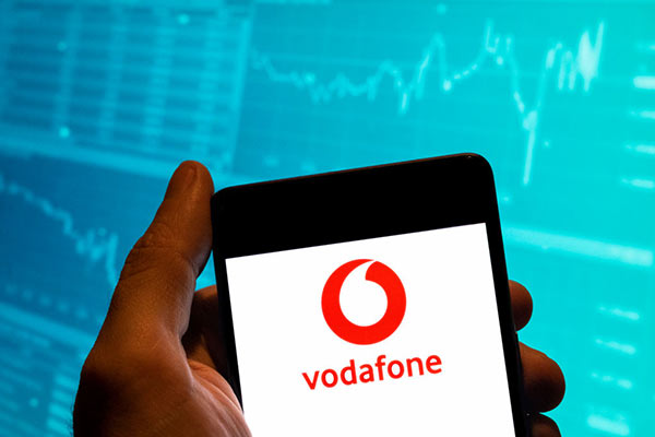 Vodafone logo on a mobile in front of stock market trading screen Getty 600