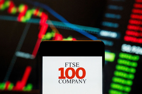 FTSE 100 logo on a smartphone against a trading screen Getty