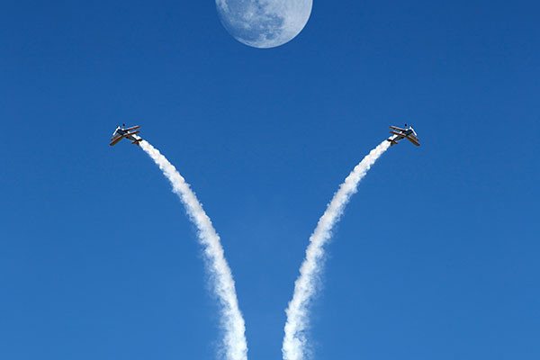 Two biplanes playing in sky with midday full moon at airshow Getty