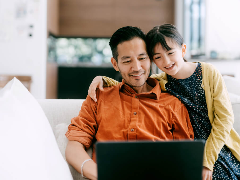 father and daughter look at laptop.