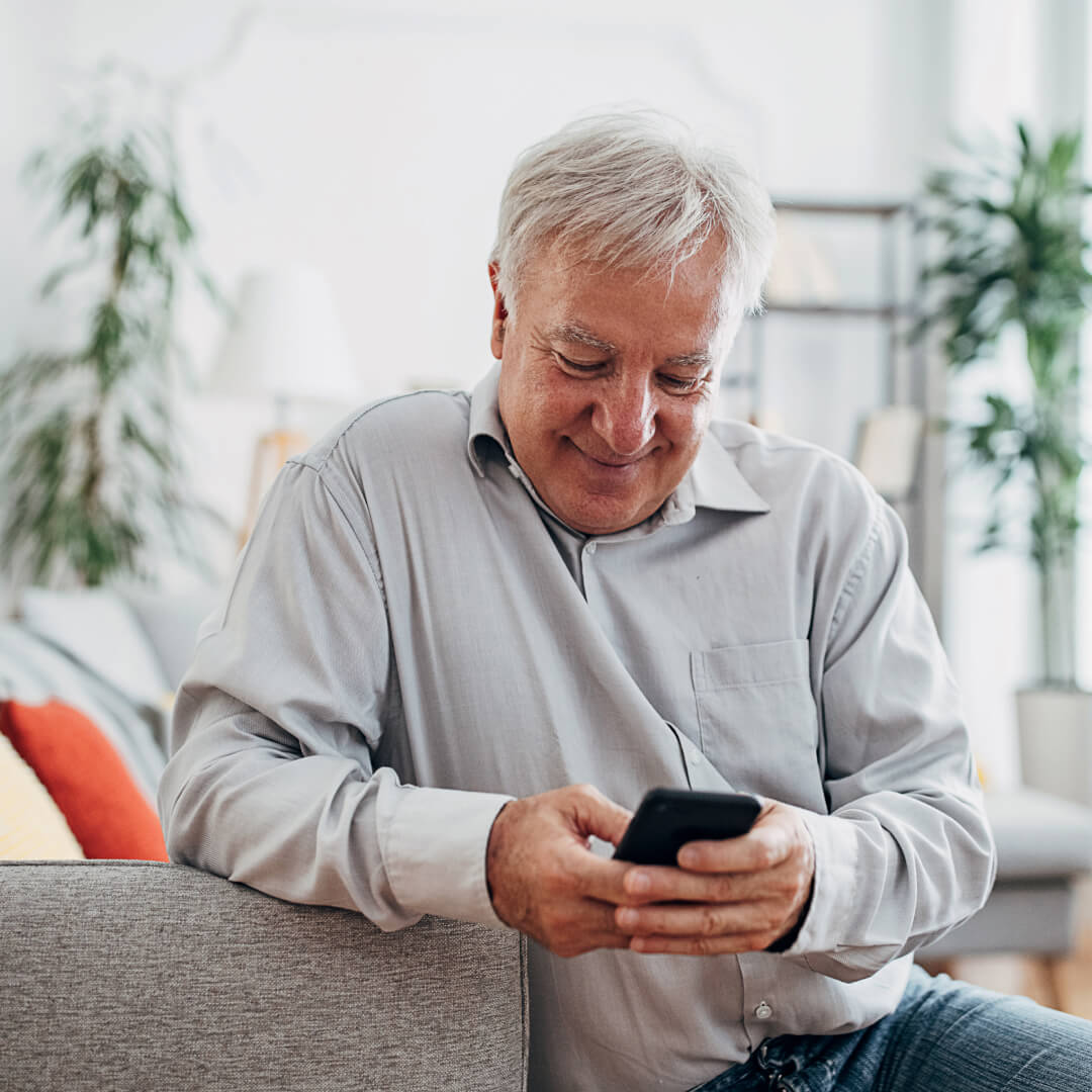 older man smiling at mobile device on sofa