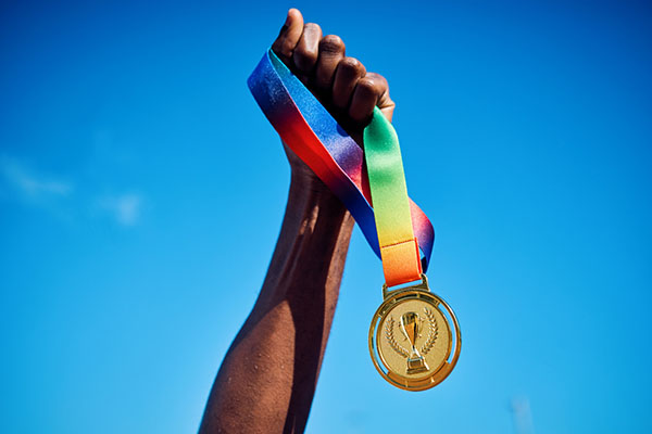 Raised hand holding a gold medal against blue sky