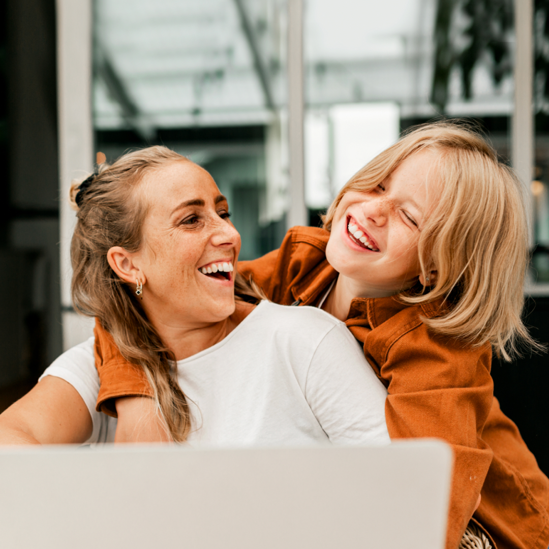 Woman smiling with child looking at laptop