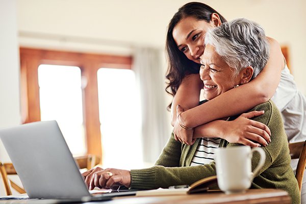 Young woman hugging her grandmother while looking at finances on a laptop Getty