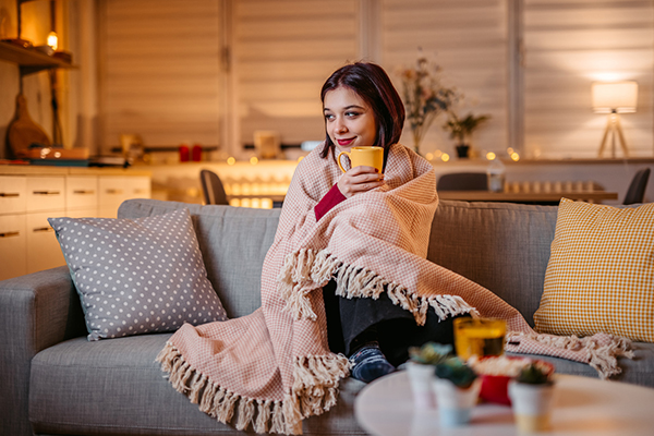 Woman curled up on a sofa with a blanket and a hot drink