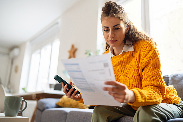 A man in a yellow jumper looking at her smartphone and a bill