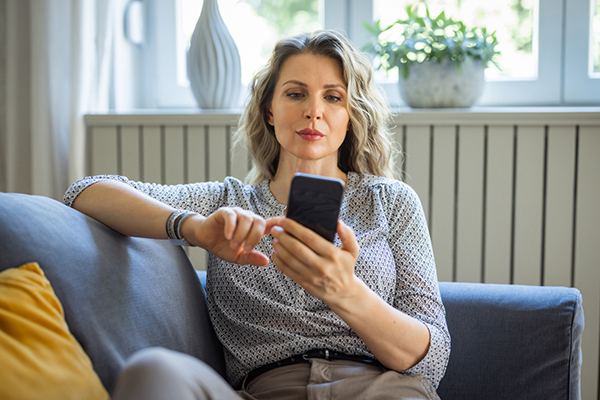 A woman sitting on sofa and using smartphone for trading online