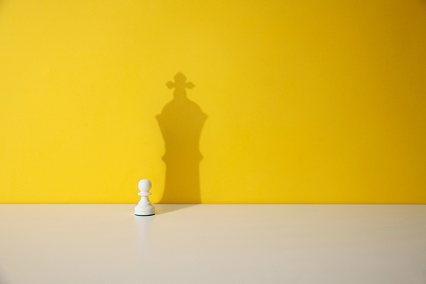 Chess pawn piece with king shadow behind it