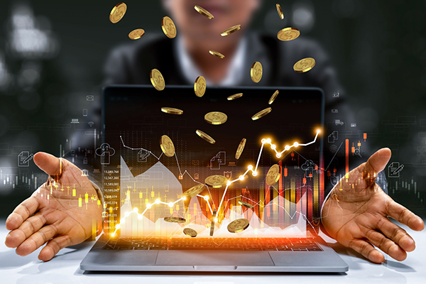 Gold coins tumbling out of a computer screen showing a financial chart, Getty