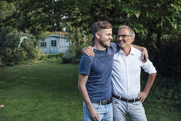 Father and son with arms around each other standing in the garden, Getty