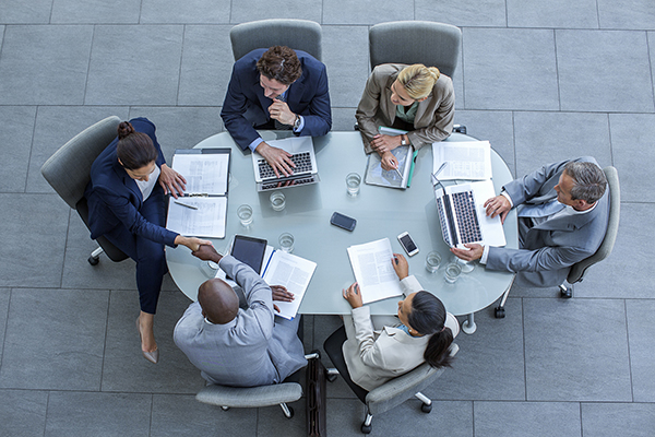 Individuals gathering around a meeting table, Getty