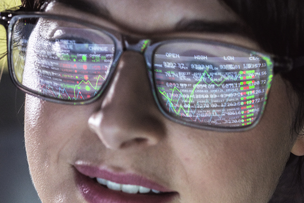 A close-up of an investor's face with figures reflected in their glasses, Getty