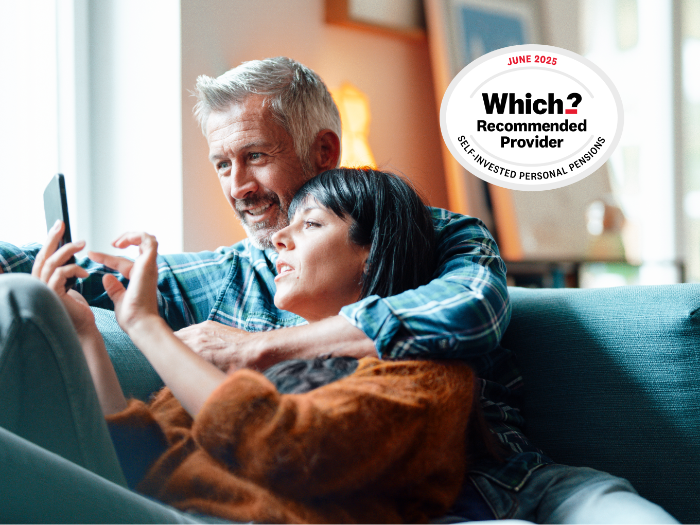 A couple in their 40's sat cosily on a couch, smiling at a mobile phone. Alongside, a Which? Recommended Provider for SIPP 2025 award badge.