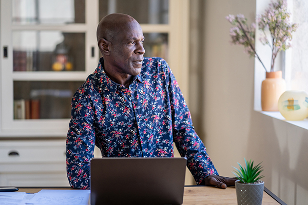 A man at a desk with a laptop, looking out of the window and thinking