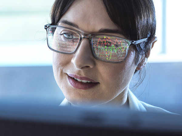 Woman looks at a monitor, her spectacles reflecting graphs and data, Getty