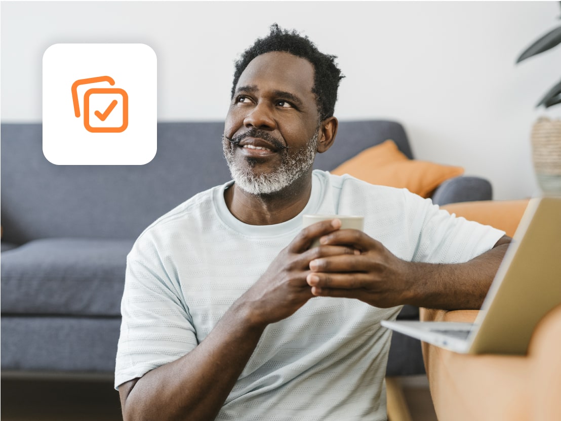 This is a man on his laptop on the sofa with a mug with a tick icon.