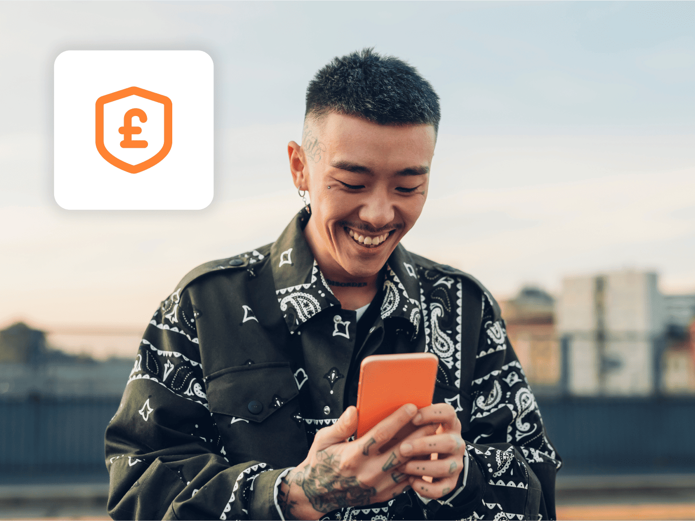 Young man in pattered shirt, smiling whilst looking at mobile. A shield with a "£" sign floats on his left. 