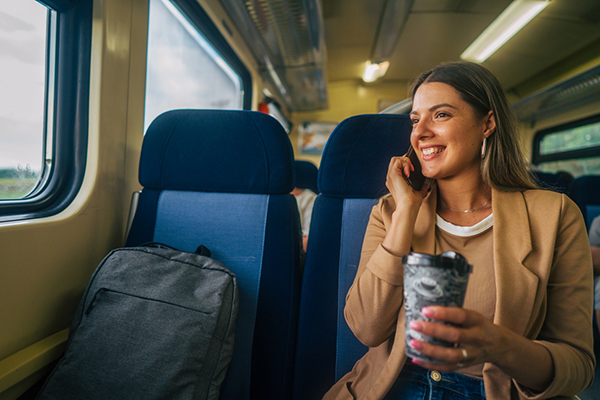 Happy woman on train with coffee talking on mobile