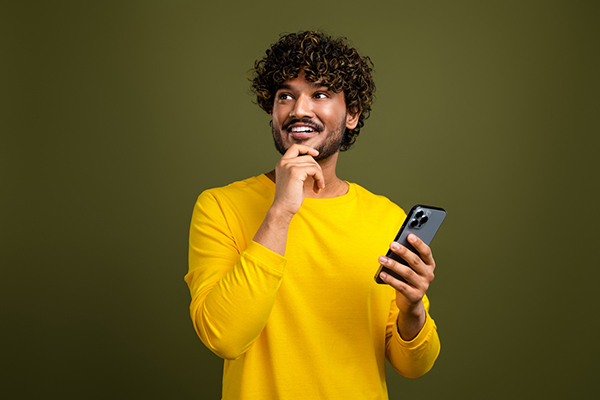 Young man holding phone and pondering share with hand to chin