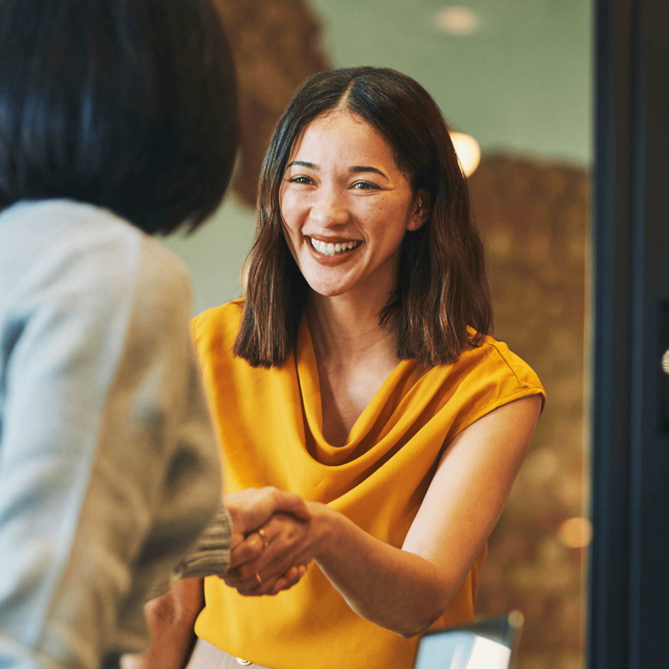 Young woman in an orange blouse smiling and shaking hands with another woman