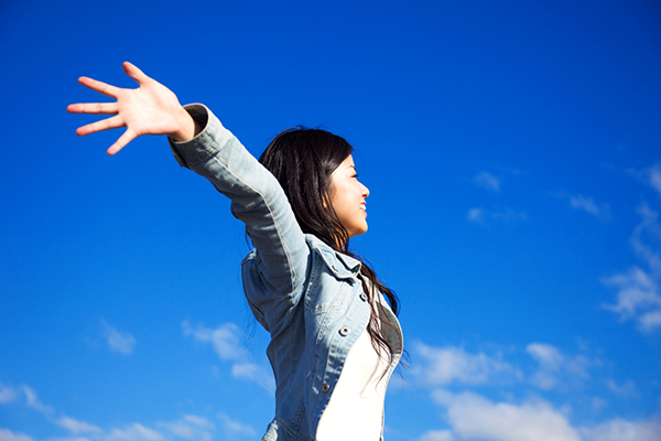 Woman breathing in air against blue sky