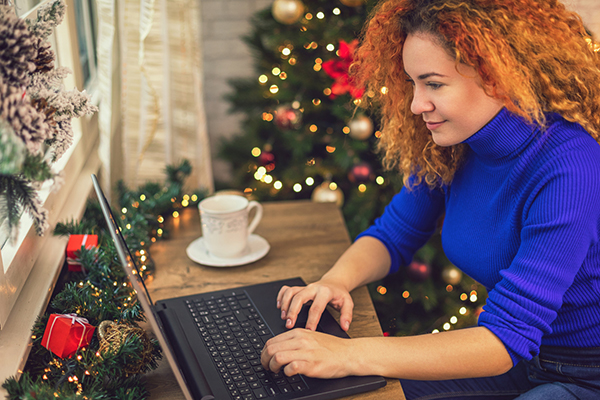 Woman working on laptop beside Christmas tree