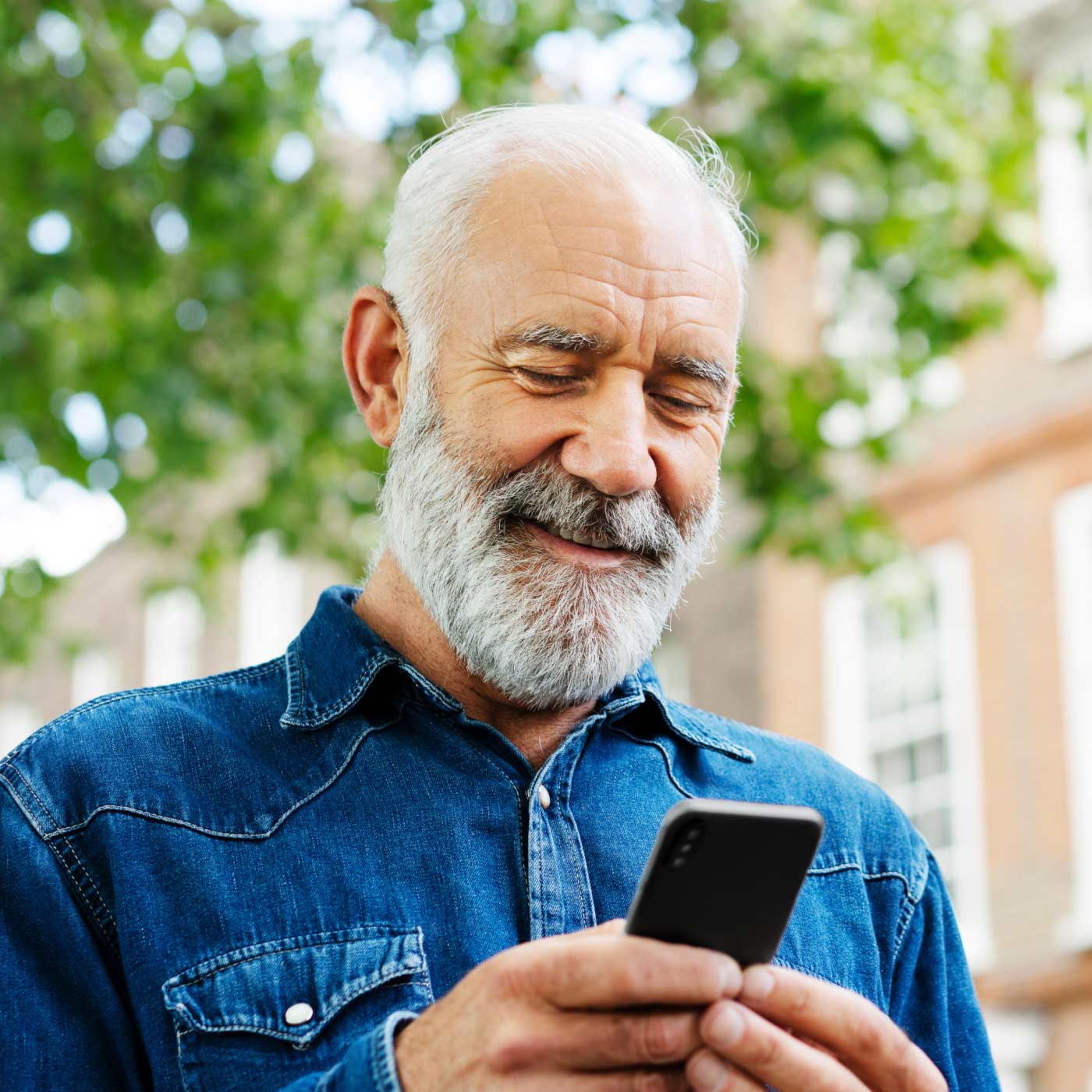 Man outdoors looking at mobile and smiling