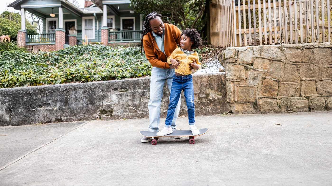 Dad and daughter playing outside riding a skateboard happily