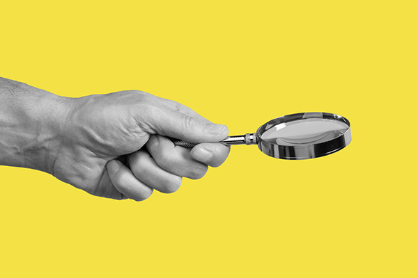 Magnifying glass and hand against yellow background