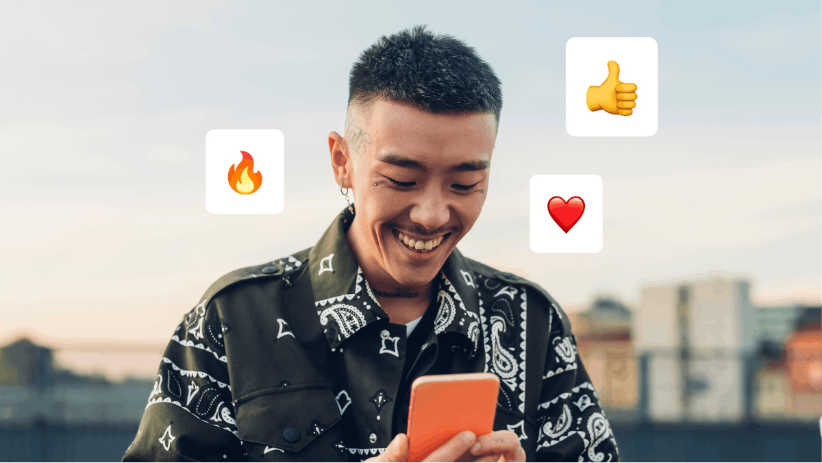 happy young man in a paisley shirt looking at his phone surrounded by positive emojis