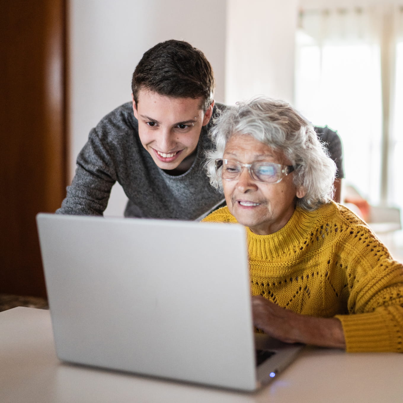 A young man and an elderly woman using a laptop together. 
