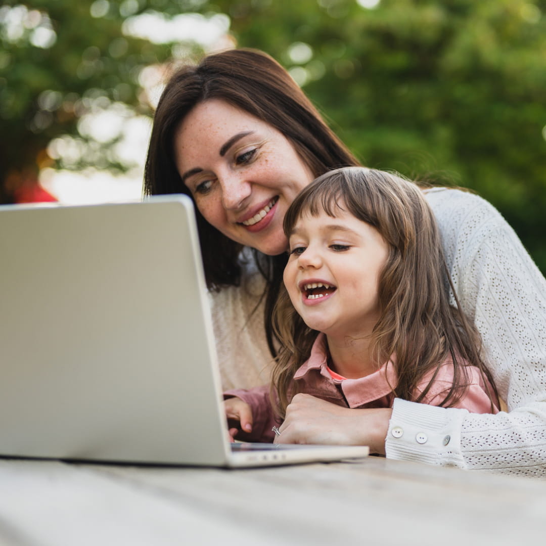 Happy mother and young daughter on laptop outside