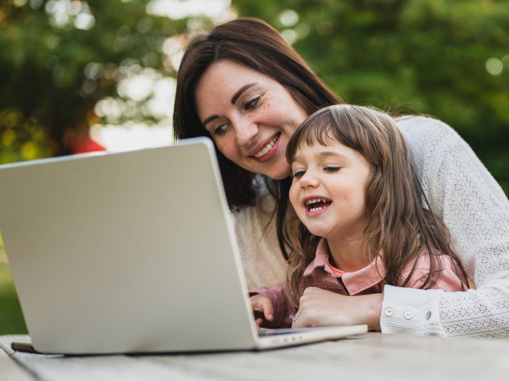 Mum and young daughter outdoors on laptop