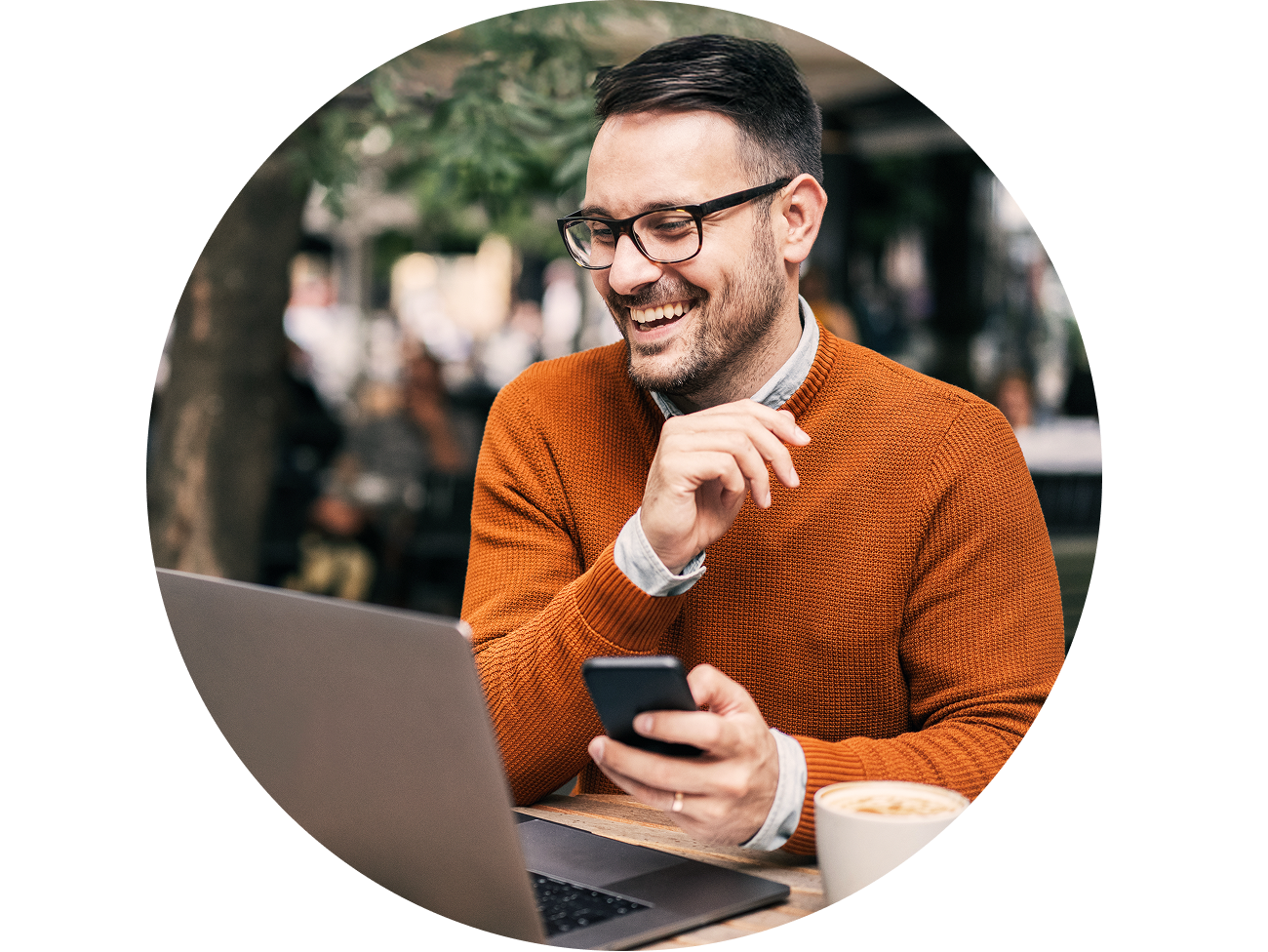 Man outside smiling at his laptop with his phone in his hand