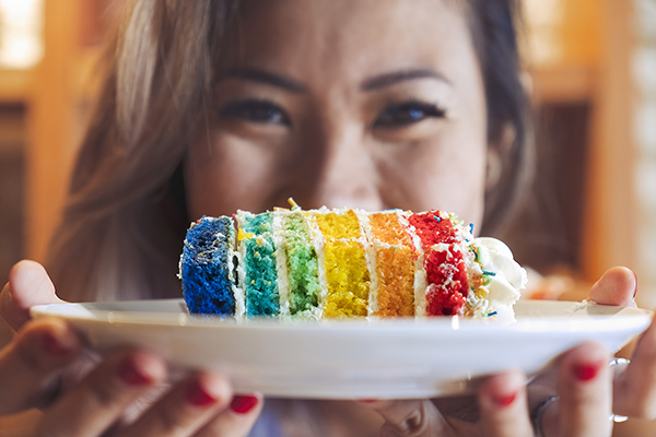 Woman offering up slice of rainbow cake