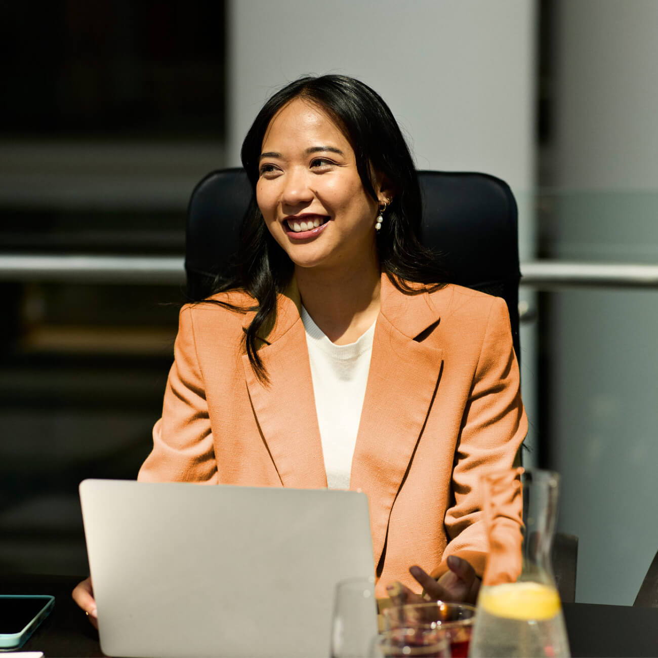 young woman in office meeting laptop smiling orange blazer